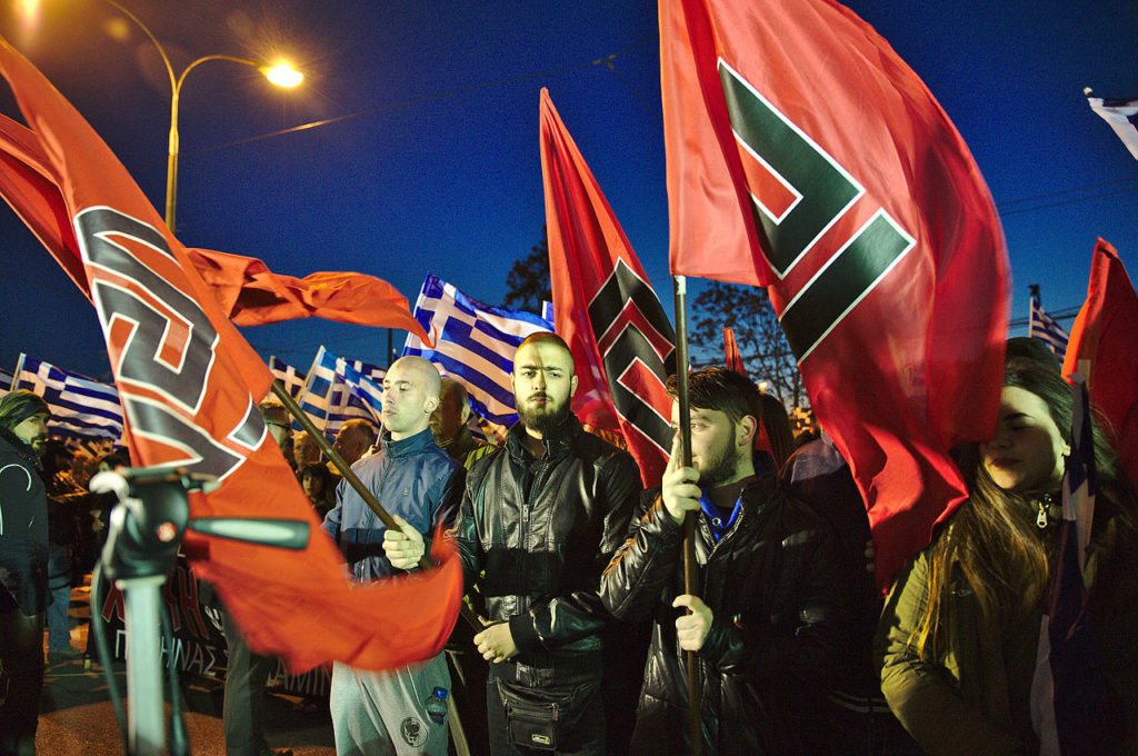 Miembros de amanecer Dorada sostienen banderas en un mitin fuera de la sede general del partido en Atenas, 2015. Autor: DTRocks, 21/03/2015. Fuente: Wikimedia Commons. (CC BY-SA 4.0)