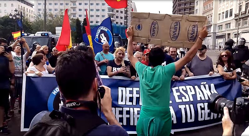 Manifestación neonazi en Madrid (en la imagen el activista rumano Lagarder Danciu —de espaldas— y la portavoz de Hogar Social Madrid Melisa D. Ruiz). Autor: canalinfoLibre, 26/05/2016. Fuente: canalinfoLibre (CC BY 2.0.)