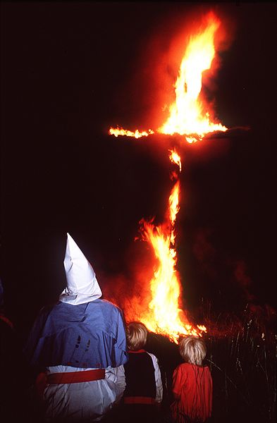 El miembro del Ku Klux Klan Joe Gosiniak observa cómo una cruz arde. Le acompañan sus hijos.  Autor: Paul M. Walsh, 1987. Fuente: Wikimedia Commons (CC BY-SA-3.0.)